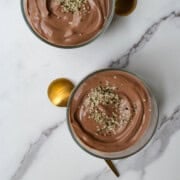 Tofu mousse (chocolate) topped with hemp hearts in two glass jars with spoons.