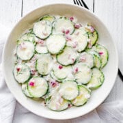 Creamy vegan cucumber salad in a white bowl with red onion and dill. Dairy-free.