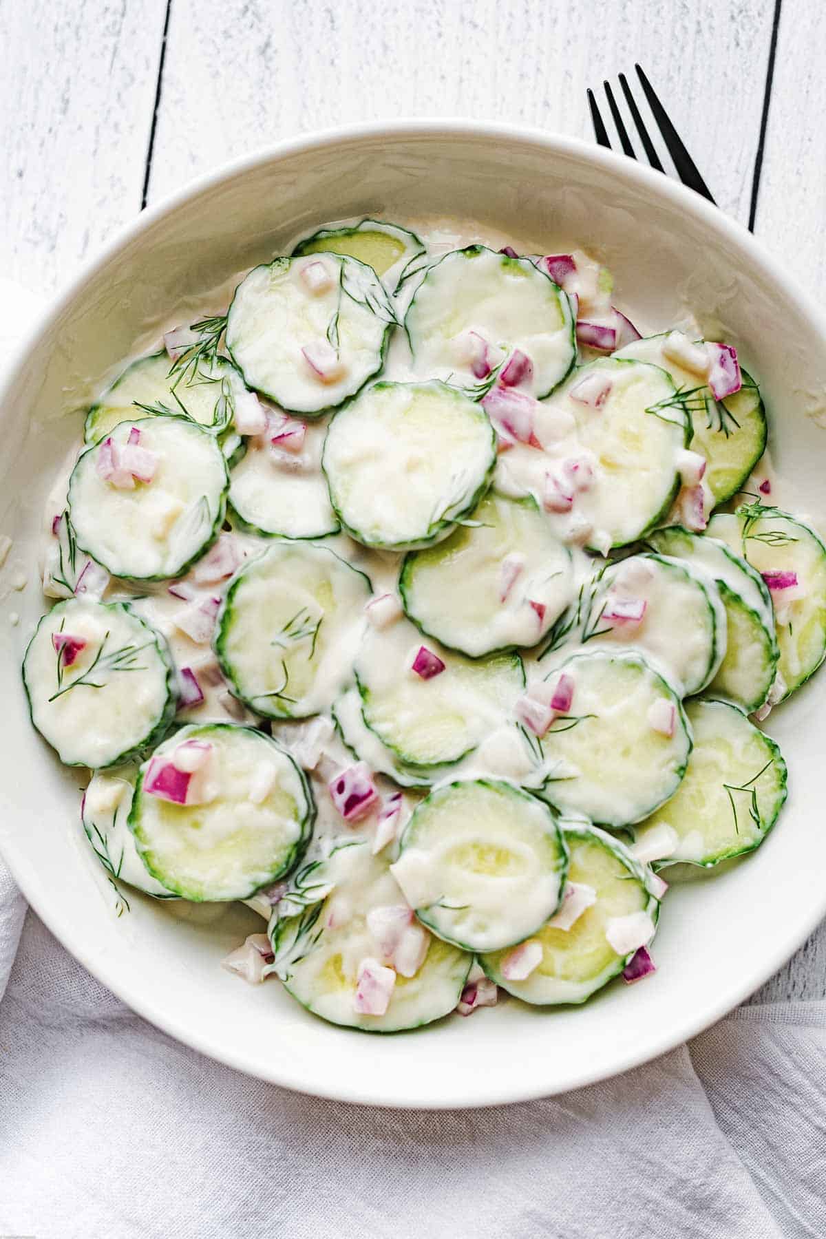 Creamy vegan cucumber salad in a white bowl with red onion and dill. Dairy-free.