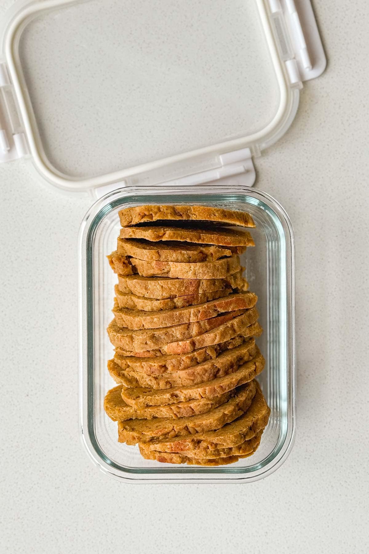 Cooked seitan sliced thinly in a glass container with a lid.