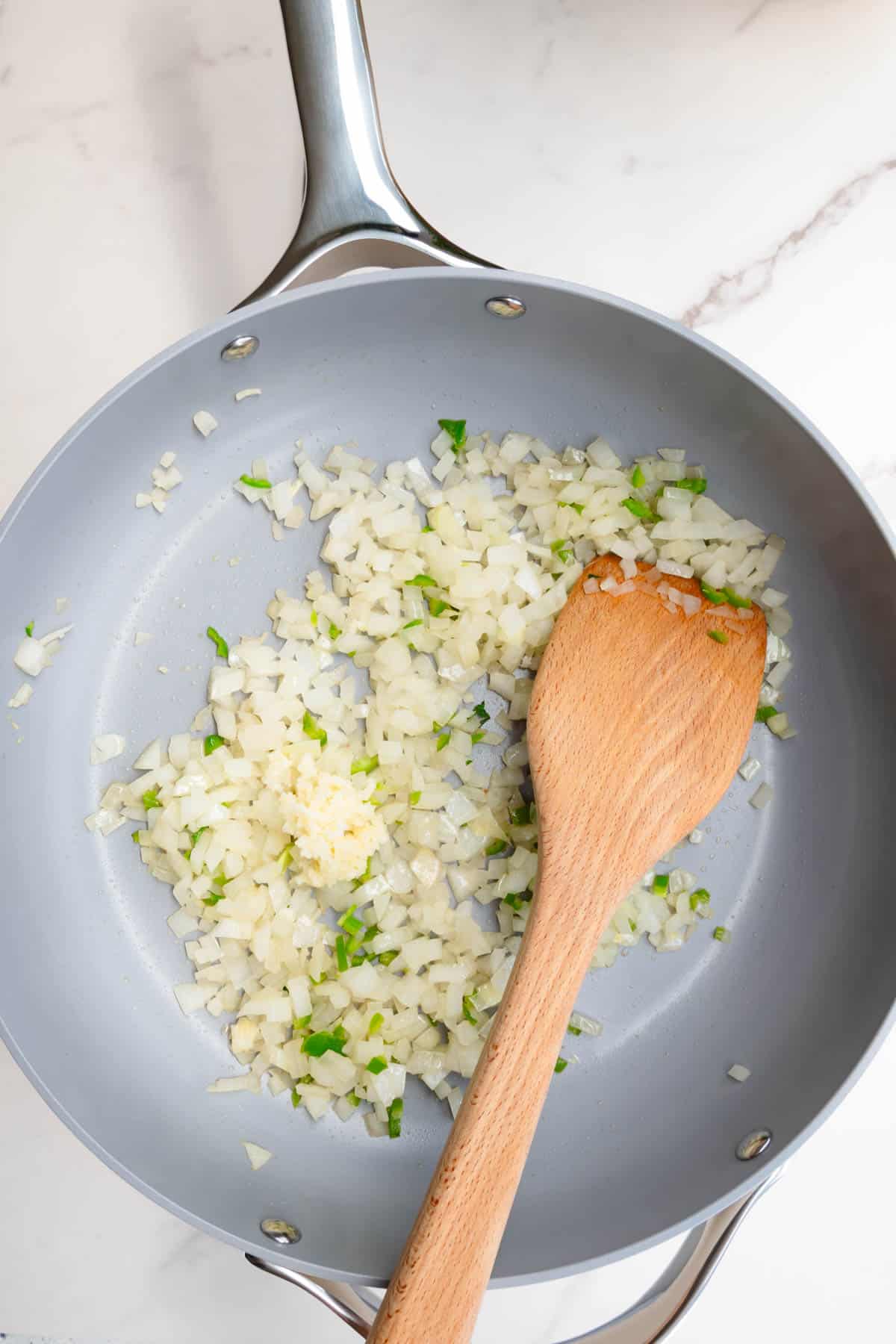 Cooked onion, garlic, and green chili pepper in a saucepan.