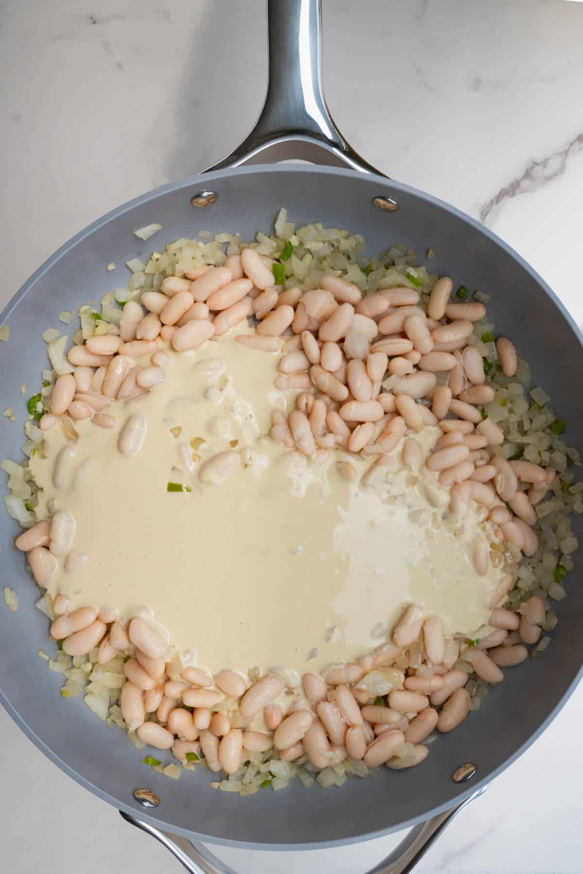 Beans, sauce, and cooked onions and garlic in a grey saucepan.