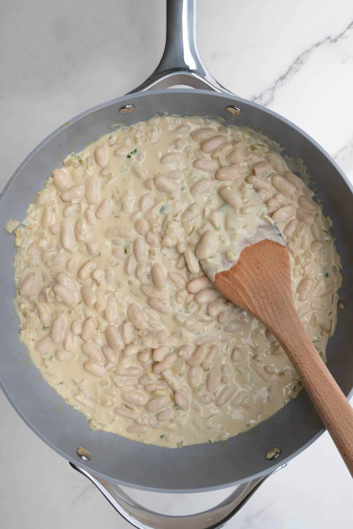 Creamy white beans with a wooden spoon in a grey skillet.