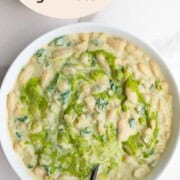 Creamy white beans with pesto in a white bowl with a black fork.