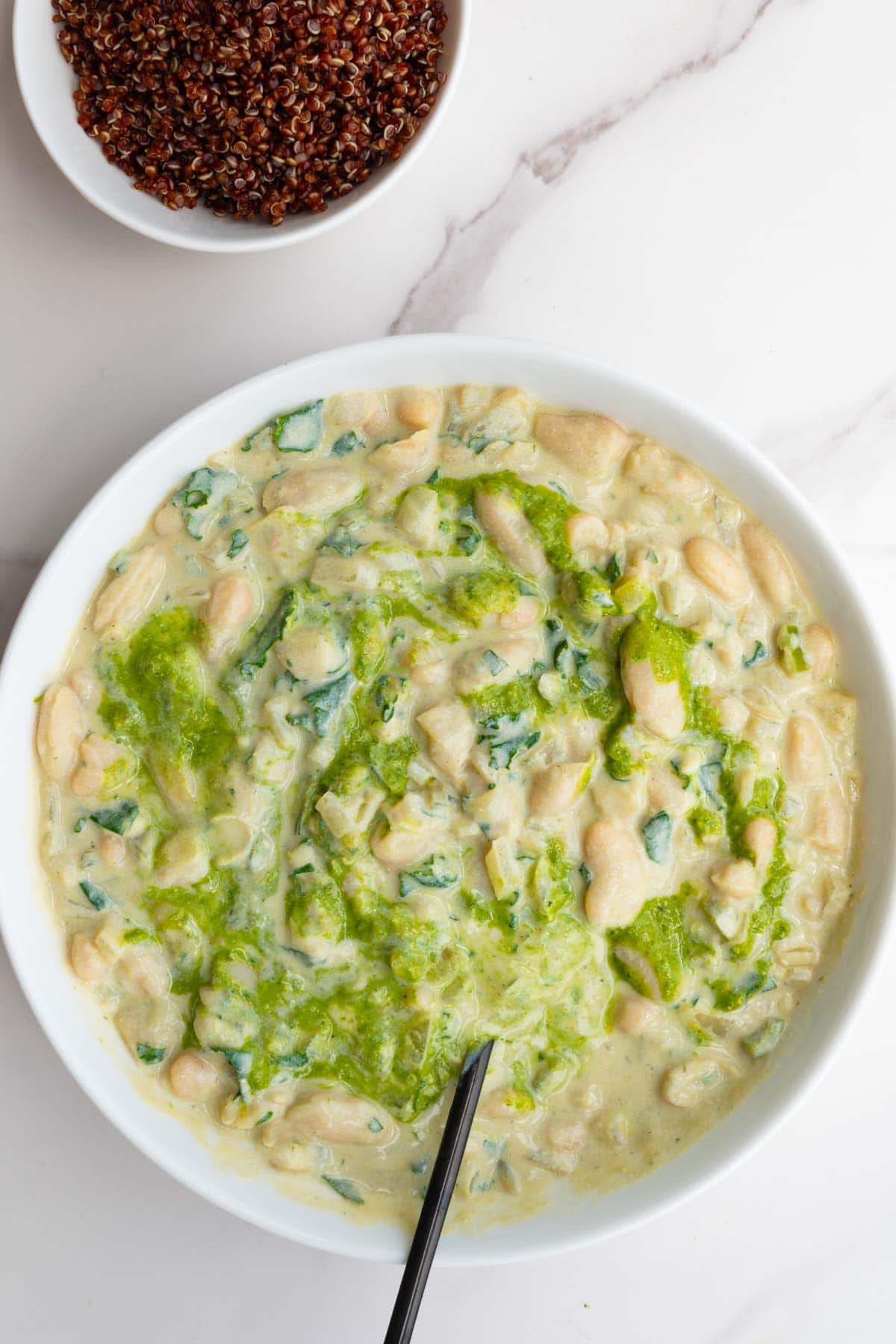 Creamy whoie beans with pesto and quinoa in a white bowl with a black fork.