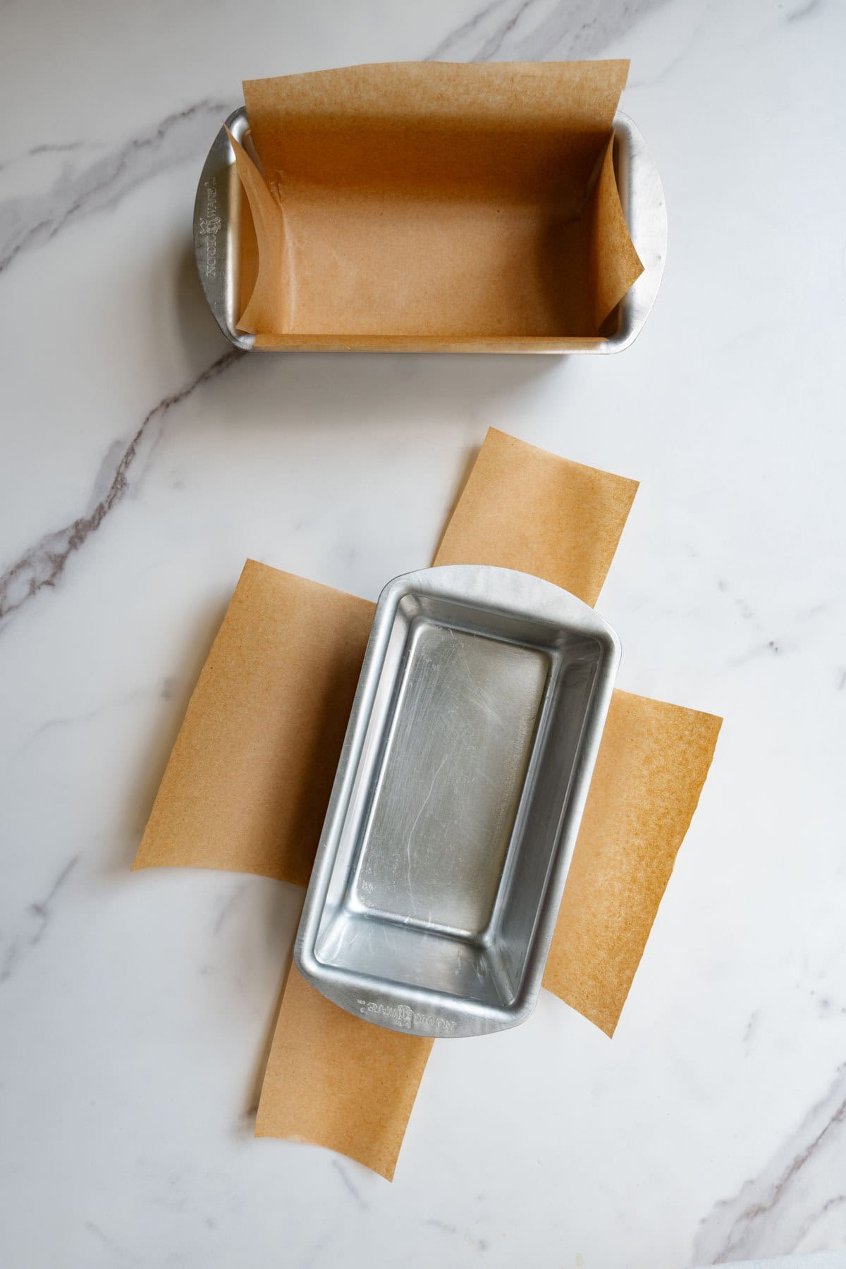 Two mini loaf pans with cut parchment paper.
