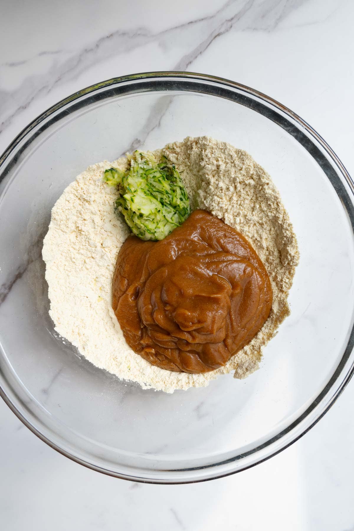 Date paste, grated zucchini, chickpea flour and baking powder in a glass bowl.