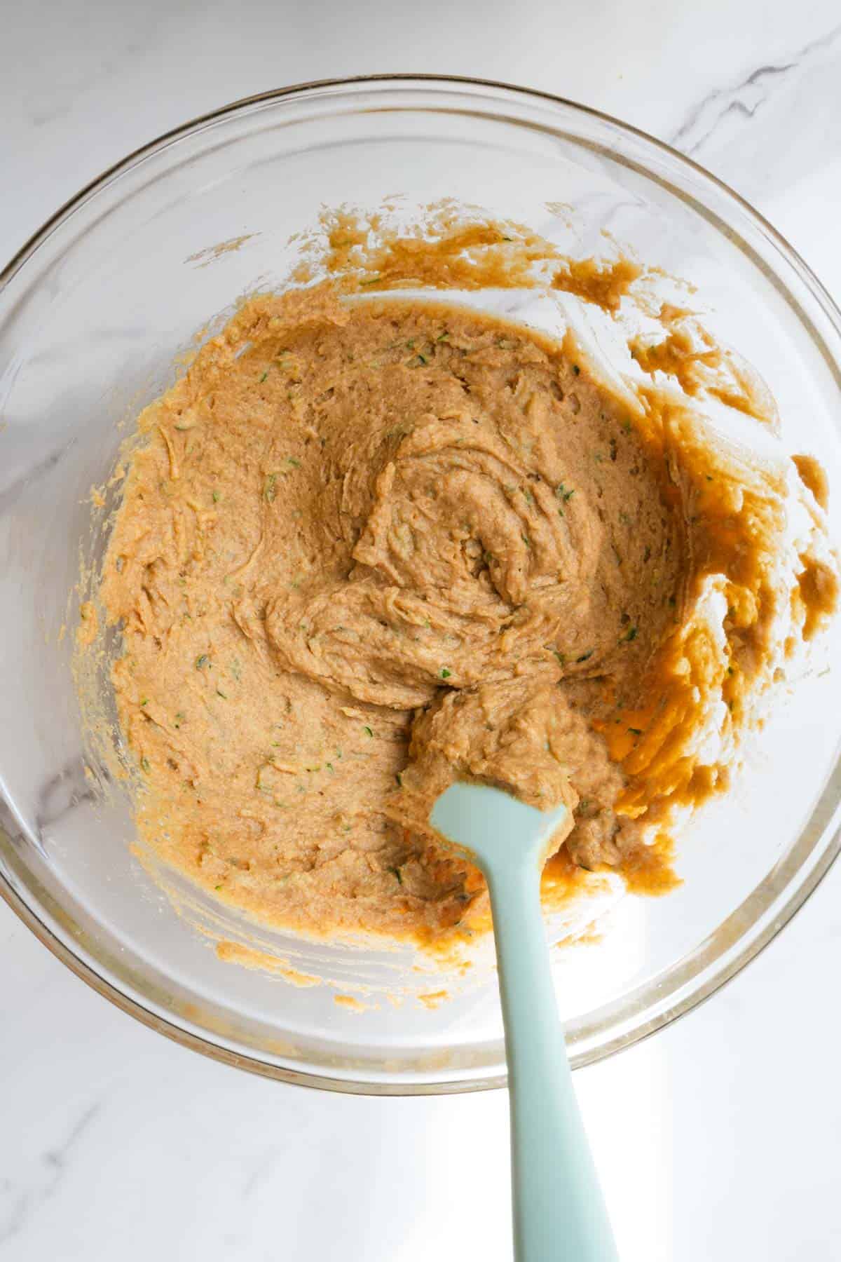 Batter in a glass bowl with a turquoise spatula.