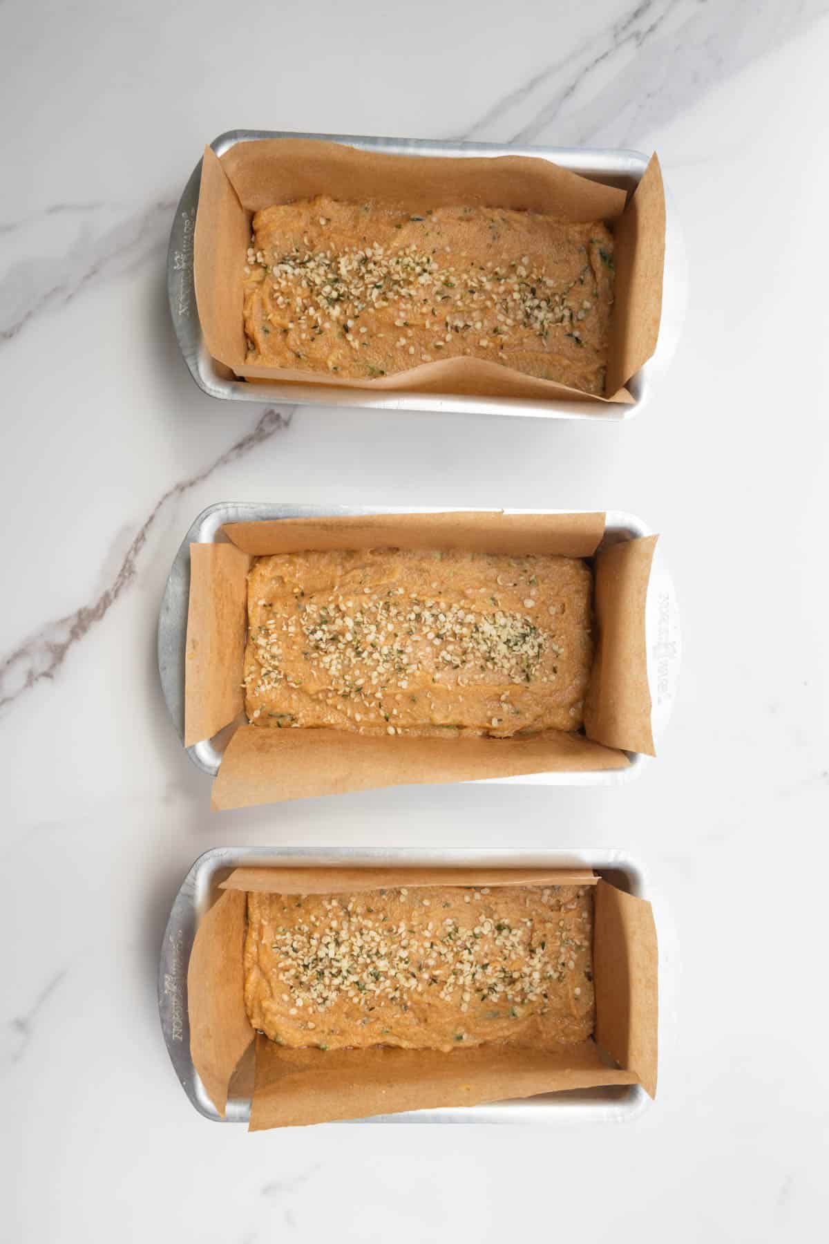 Three mini loaf pans with batter and hemp hearts.