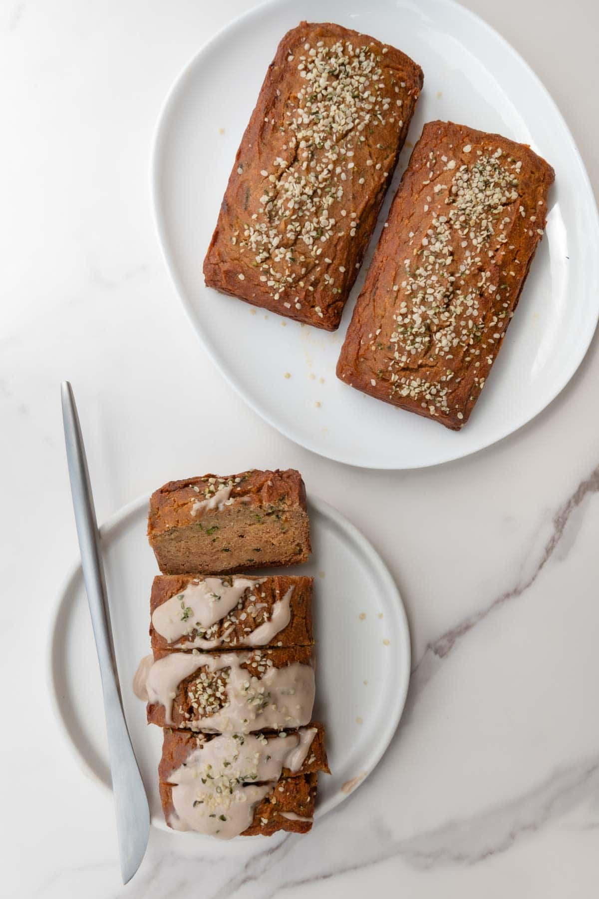 Gluten-free zucchini bread sliced on a white plate next to two more loaves.