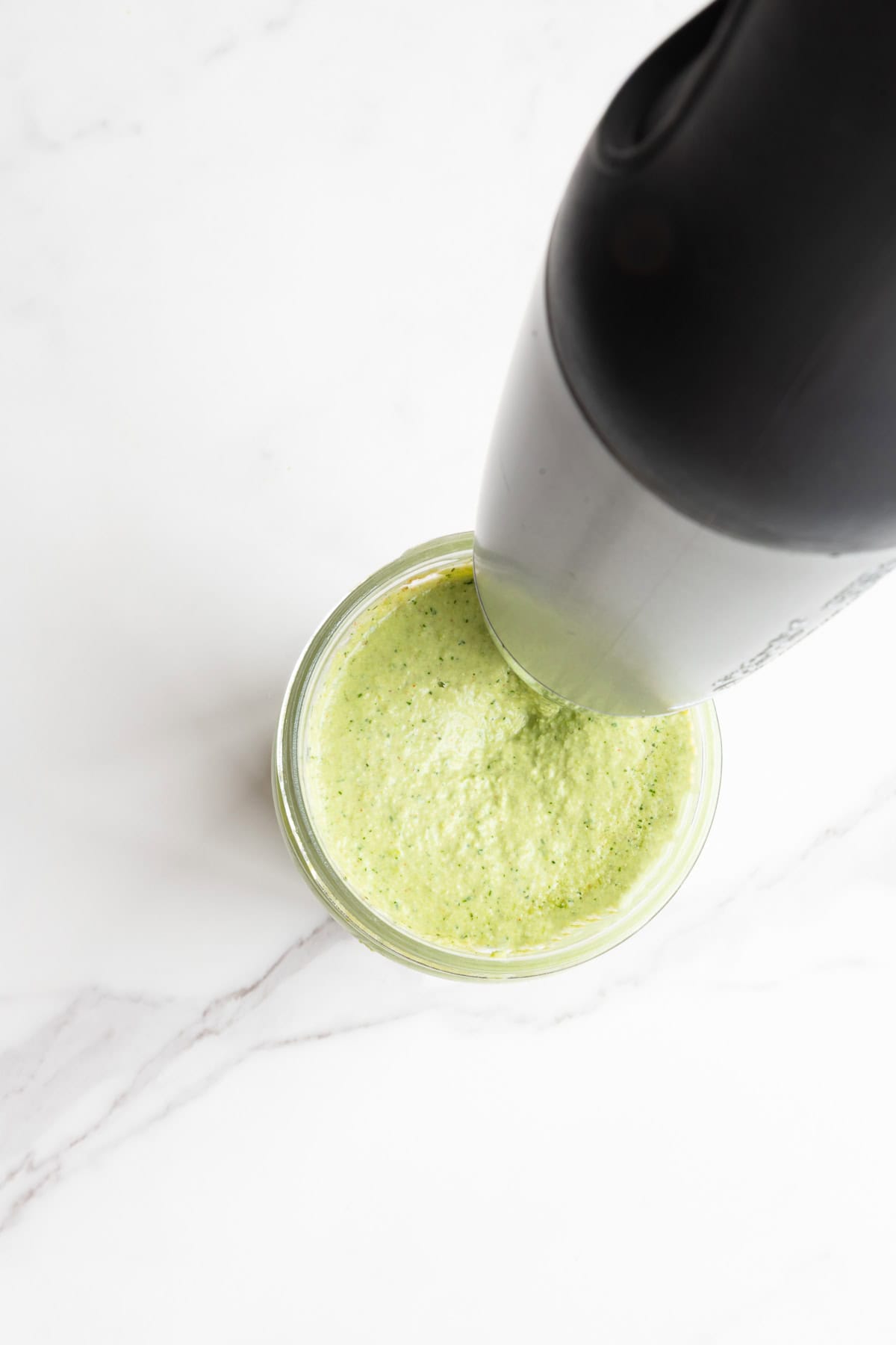 Immersion blending a green spread in a tall glass jar.