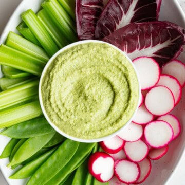 Greek Green Goddess Dip on a white platter with crudités.