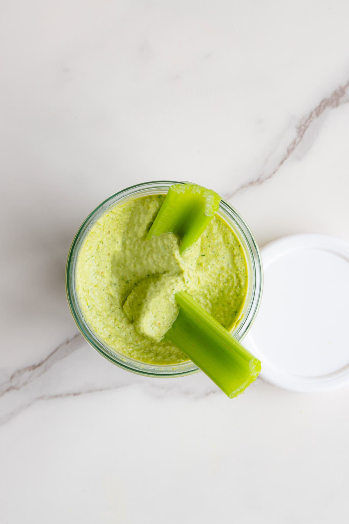 Greek green goddess dip in a glass storage jar with celery.