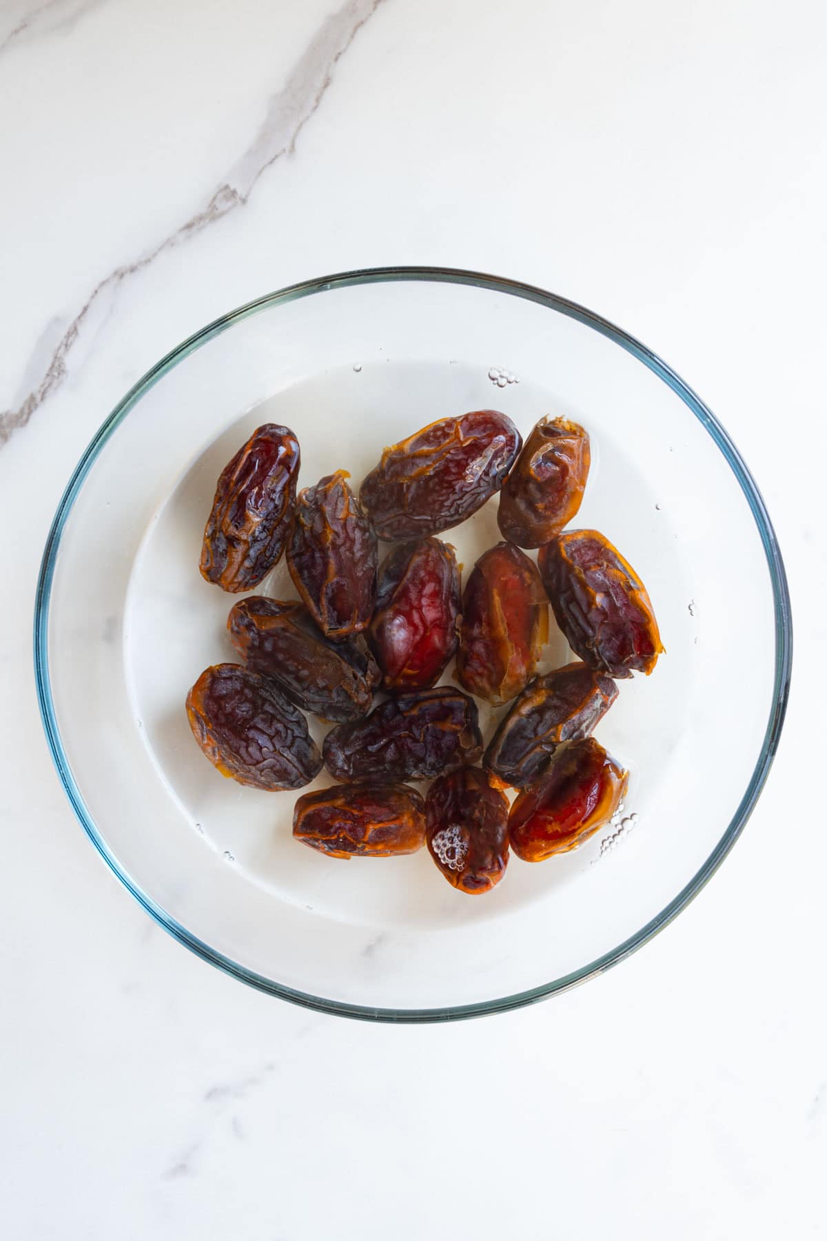Dates soaking in hot water in a glass bowl.