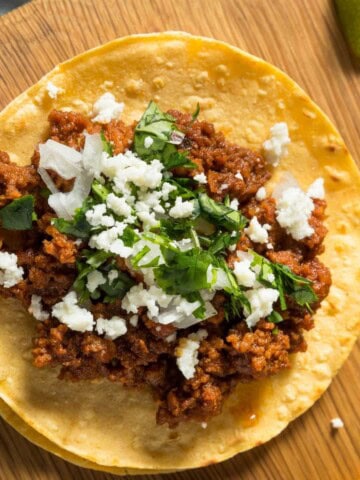 Tofu taco meat on tacos with vegan feta and chopped fresh herbs.