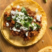 Tofu taco meat on a corn tortilla topped with vegan feta and chopped herbs.