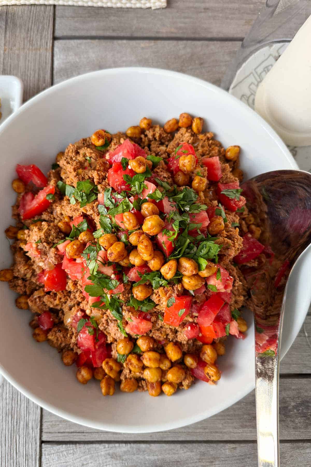 Tofu taco meat topped with roasted chickpeas and chopped tomatoes in a white bowl.
