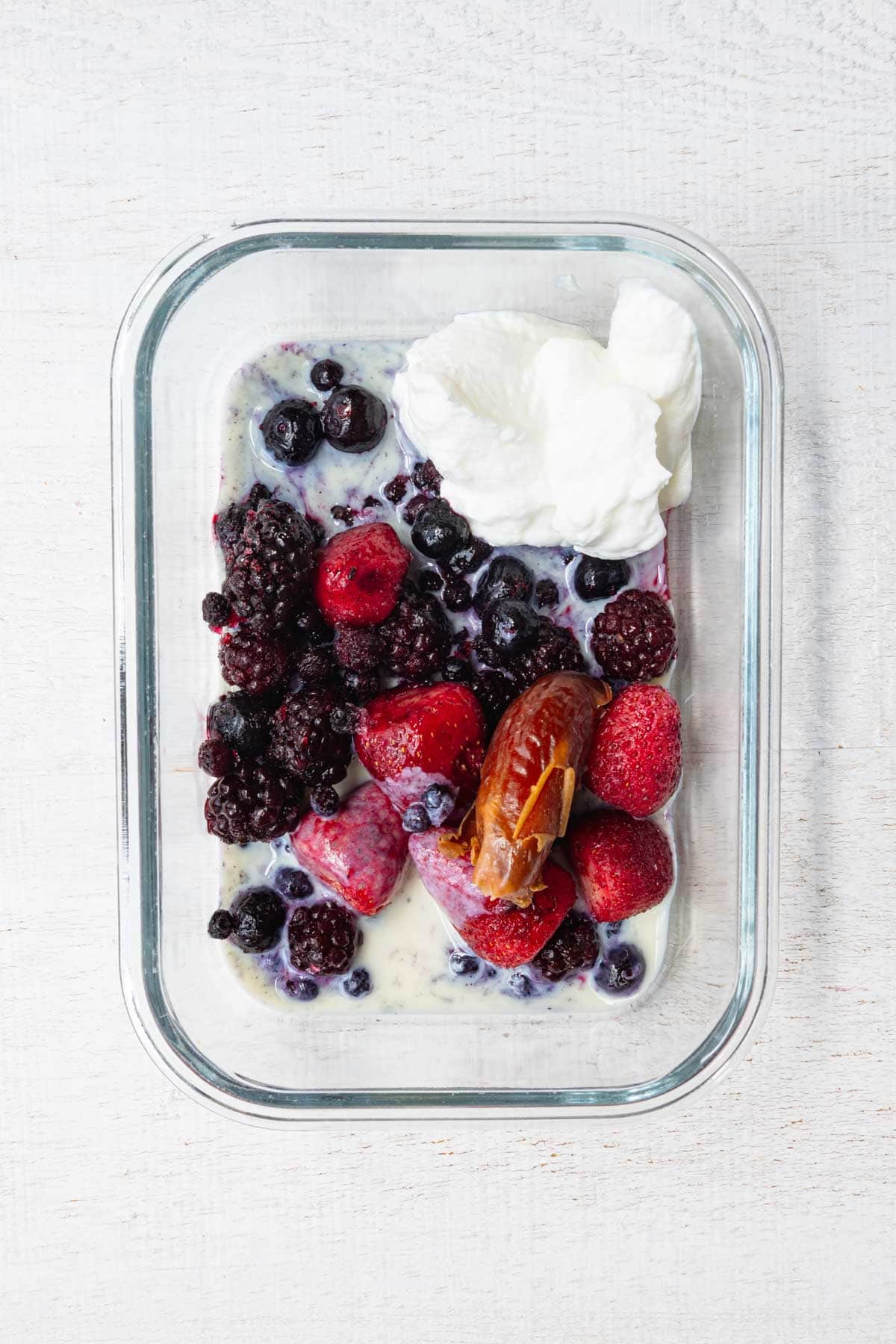 Yogurt, nondairy milk, frozen berries, and a date in a glass dish.