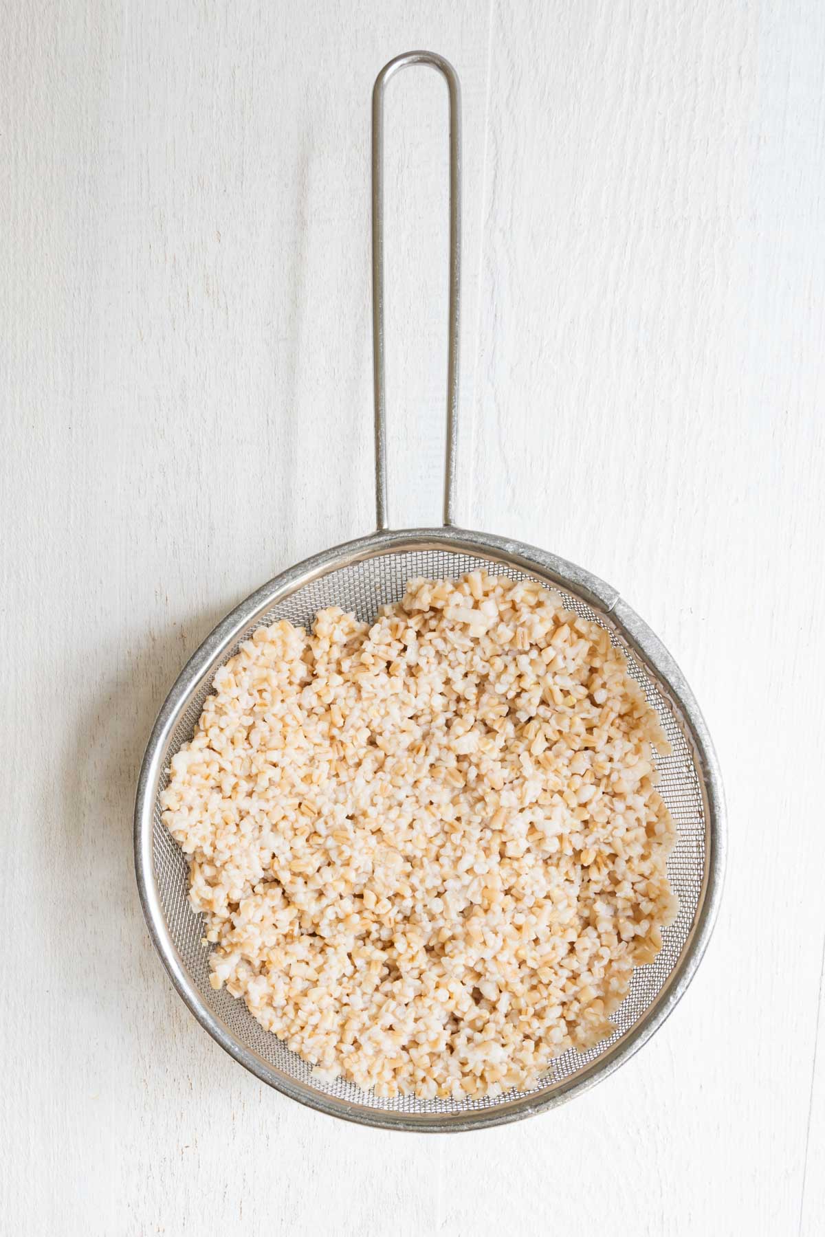 Cooked steel-cut oats in a sieve,
