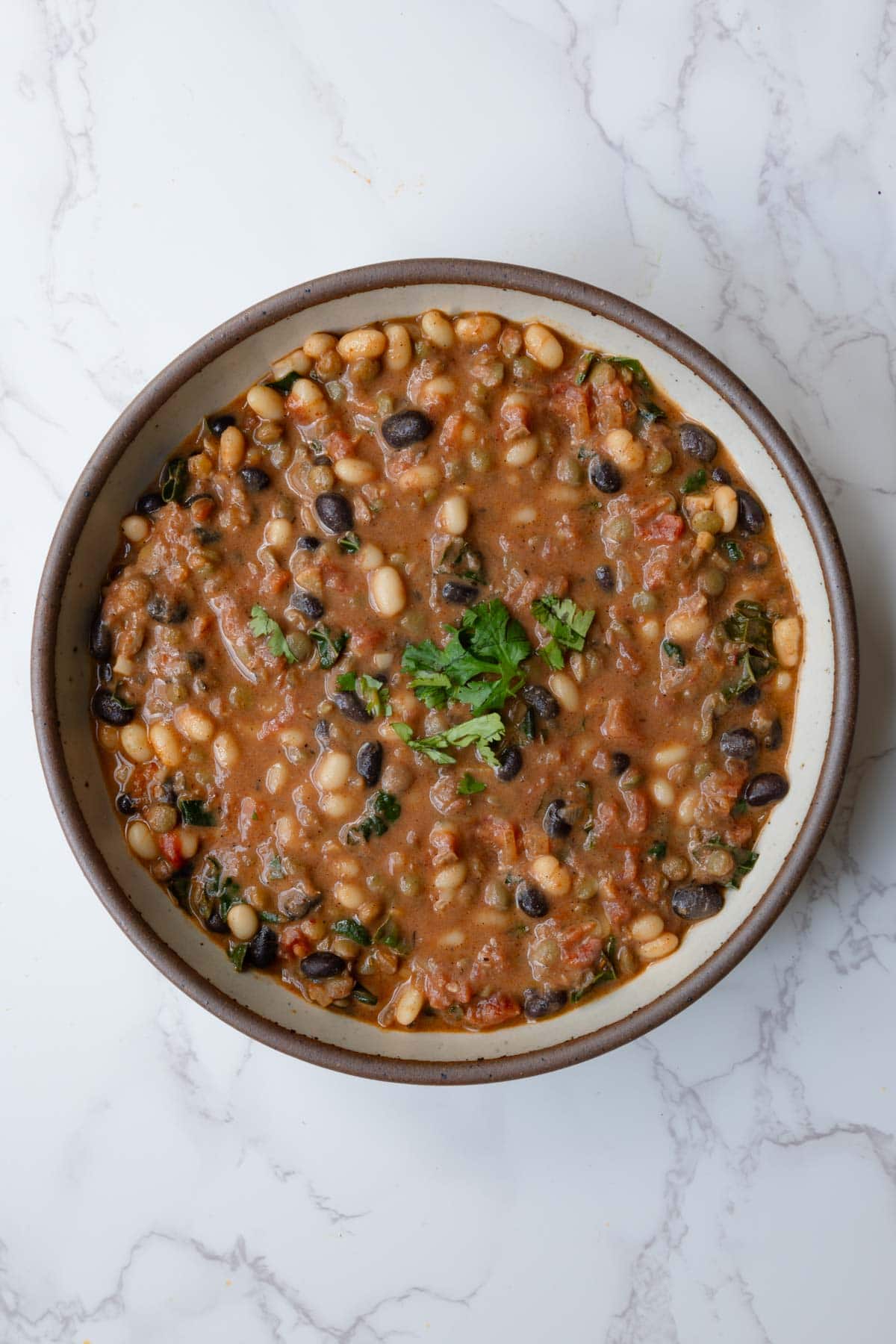 Protein chili with beans in a bowl topped with chopped fresh herbs.