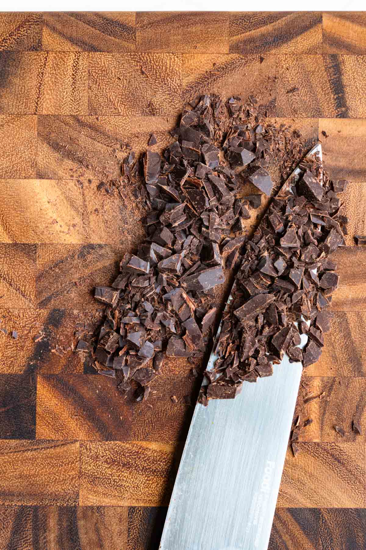 Chopped dark chocolate on a wooden cutting board.