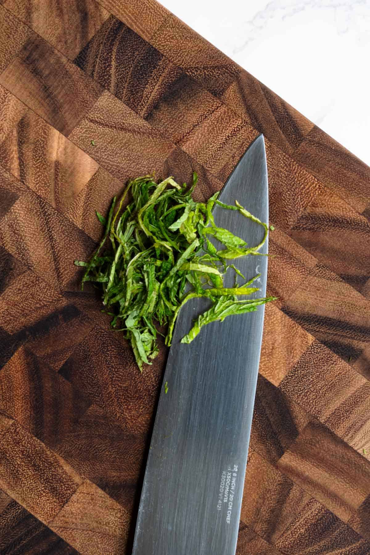 Chiffonade mint on a wooden cutting board.