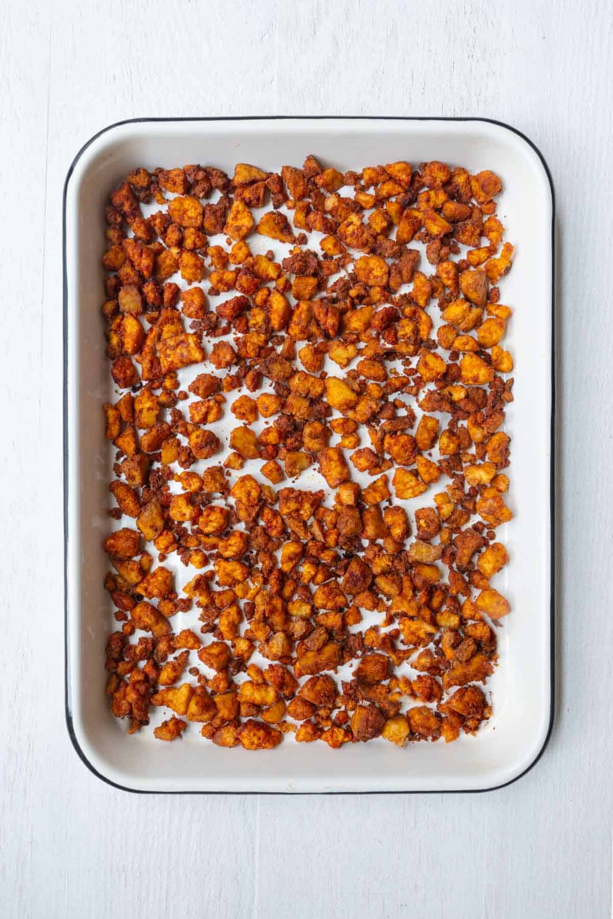 Vegan sausage crumbles on a white baking sheet.