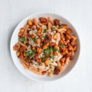 Creamy mushroom tofu pasta in a white bowl topped with chopped parsley.