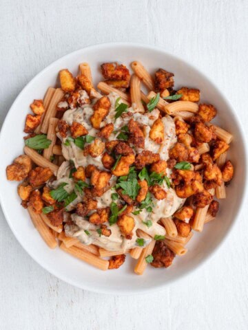 Creamy mushroom tofu pasta in a white bowl topped with chopped parsley.