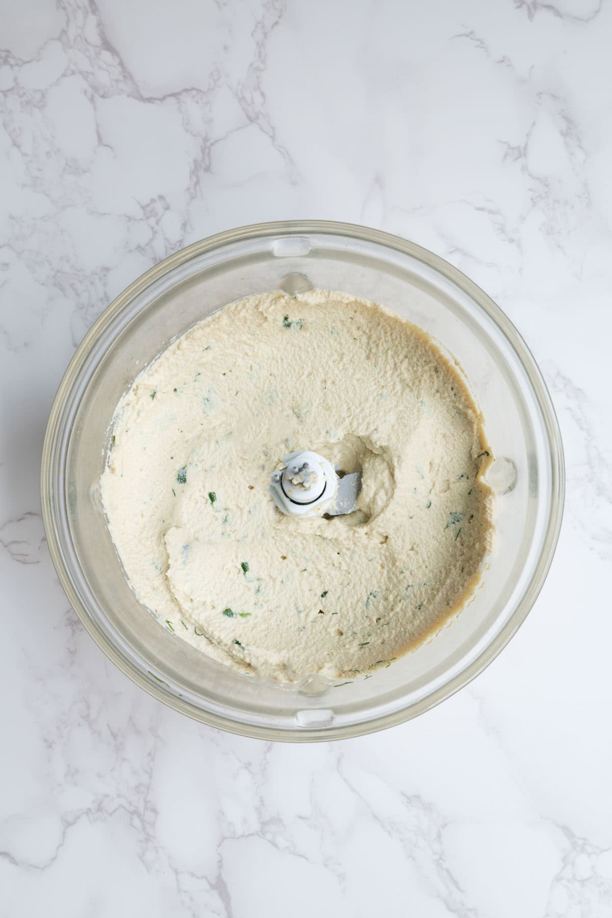 Smooth creamy spread in a food processor with chopped herbs.