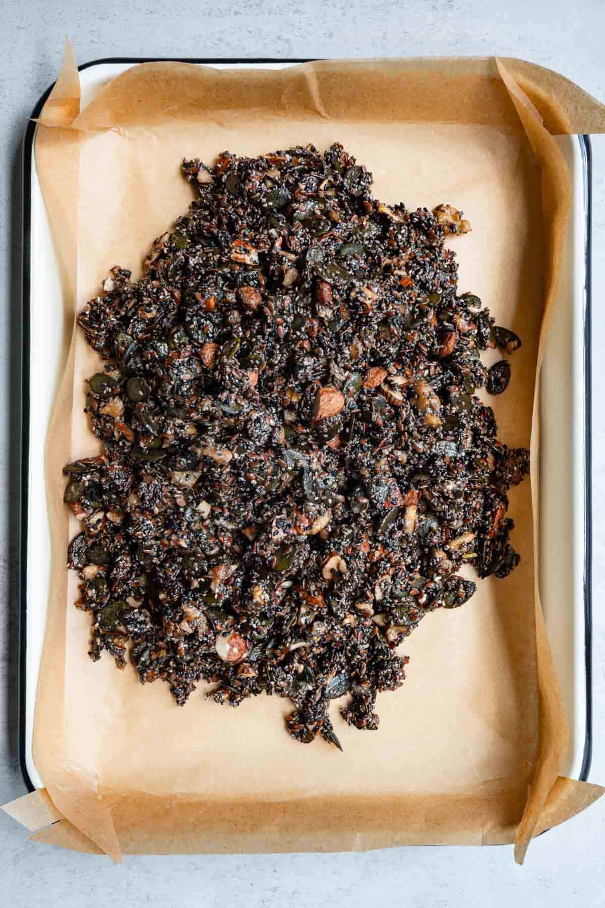 Nuts and seeds with date syrup and tahini on parchment paper in a baking sheet.