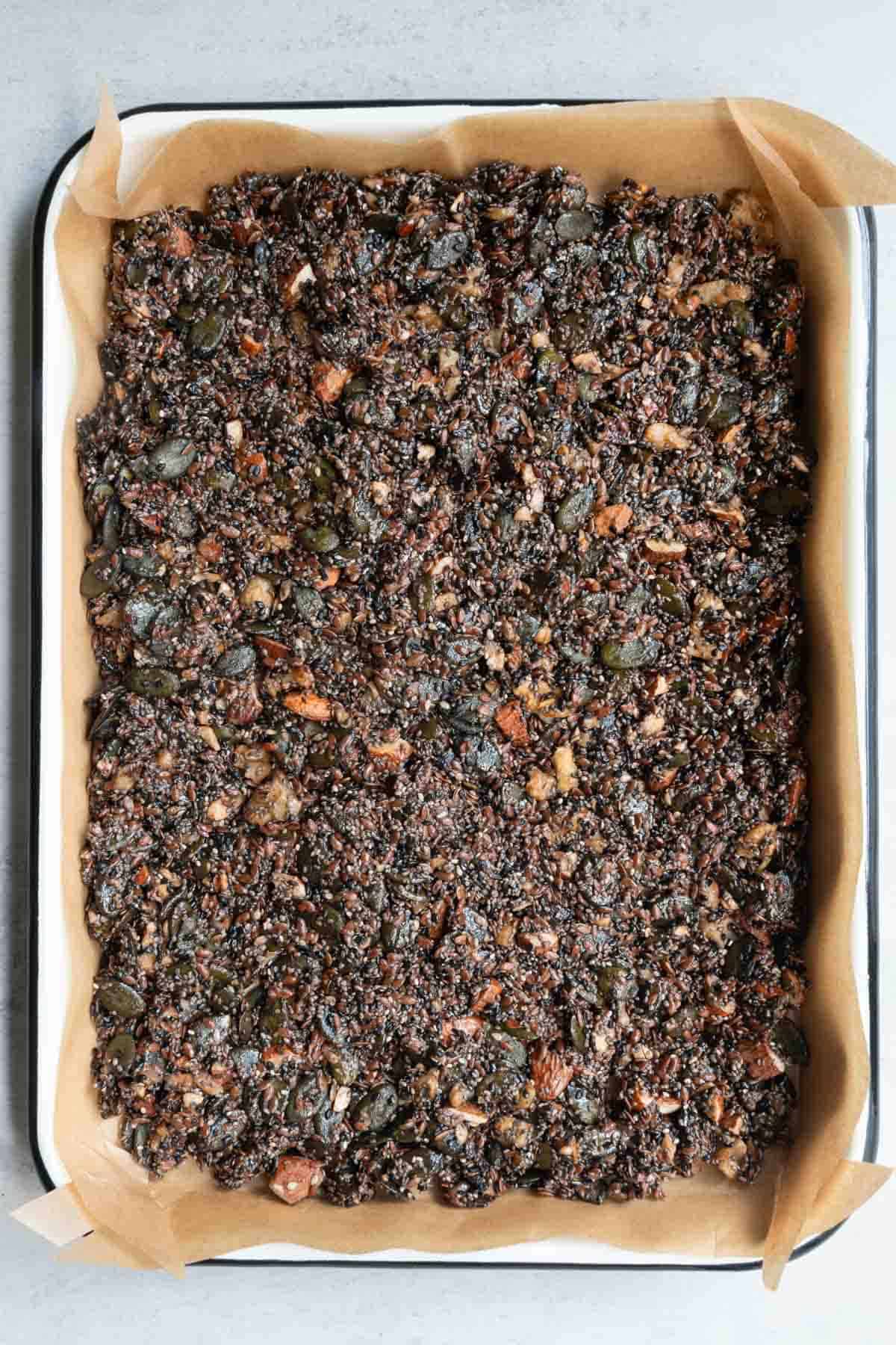 Nuts and seeds with date syrup and tahini pressed down on parchment paper in a baking sheet.