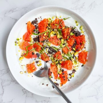 Greek yogurt bowl with orange segments, dark chocolate, mint, and pistachios.