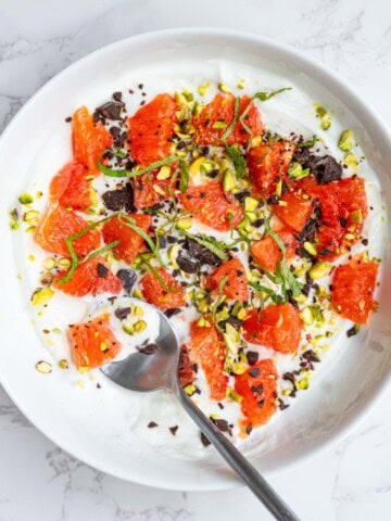 Greek yogurt bowl with orange segments, dark chocolate, mint, and pistachios.