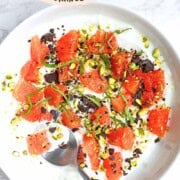 Greek yogurt bowl with orange segments, dark chocolate, mint, and pistachios.