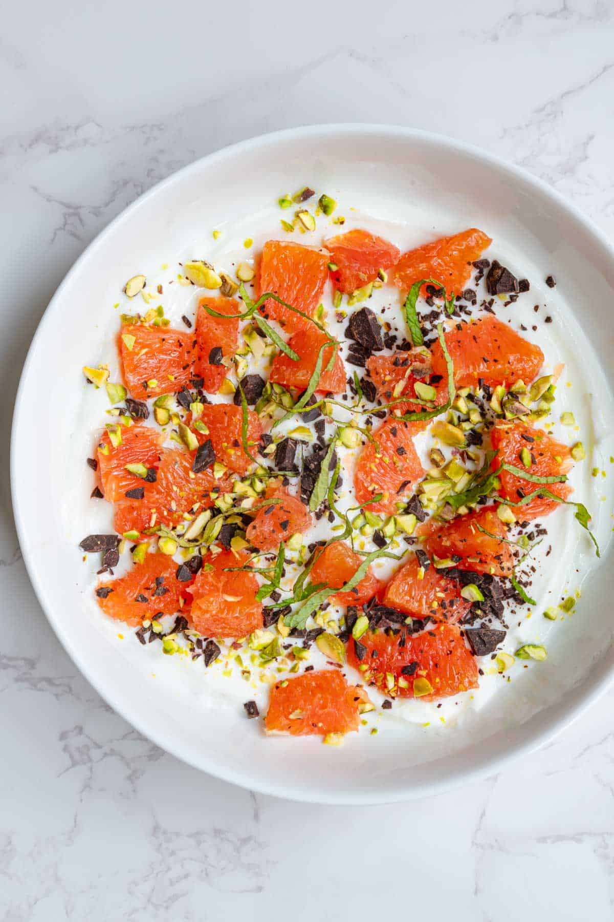 Greek yogurt bowl with orange segments, dark chocolate, mint, and pistachios.