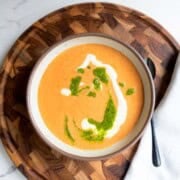 High-protein vegan soup with tomato and beans topped with pesto and vegan cream on a wooden board.