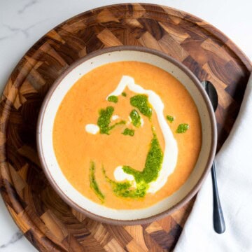 High-protein vegan soup with tomato and beans topped with pesto and vegan cream on a wooden board.