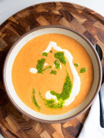High-protein vegan soup with tomato and beans topped with pesto and vegan cream on a wooden board.