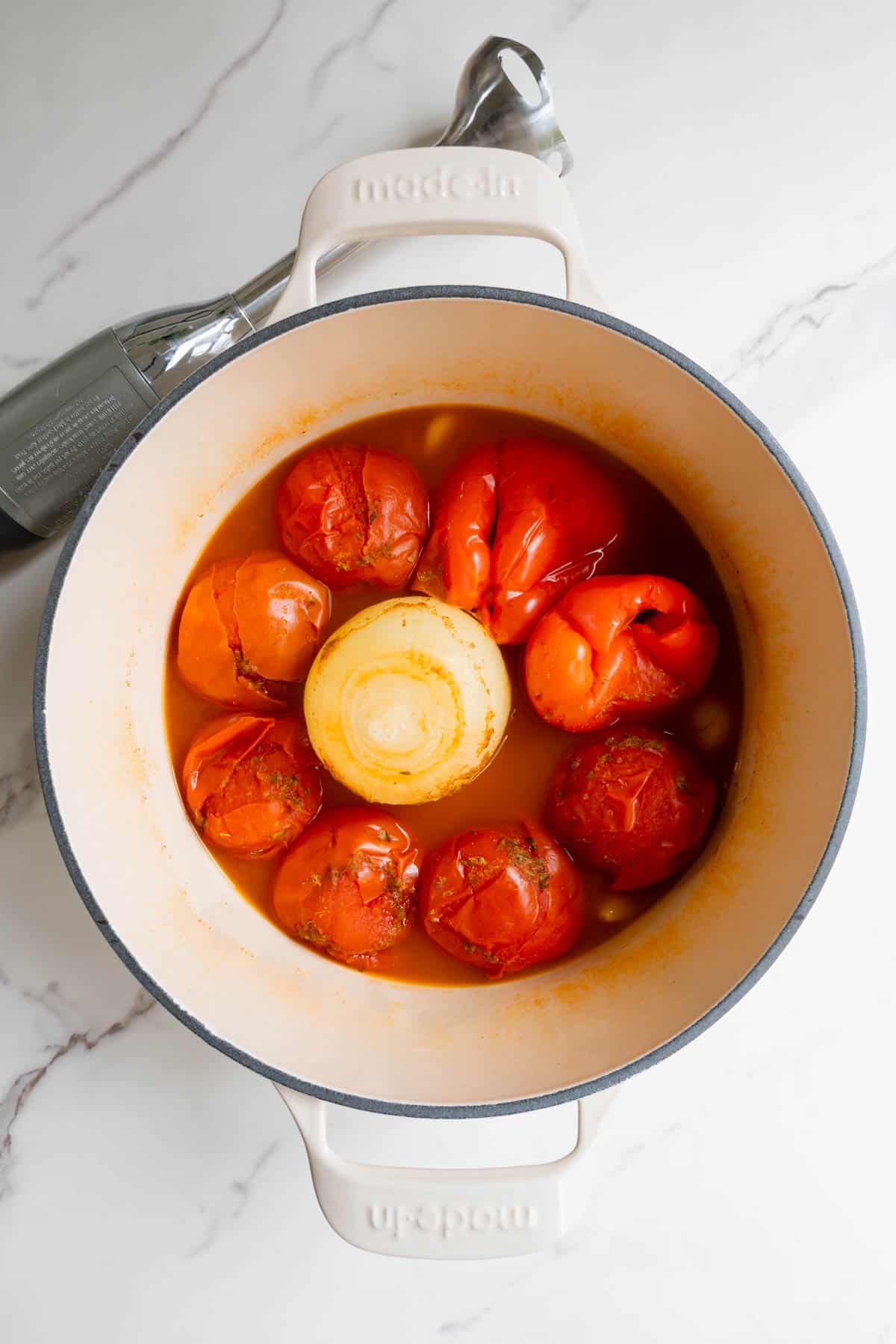 Cooked tomatoes, red bell pepper, onion, and garlic in a white saucepan.