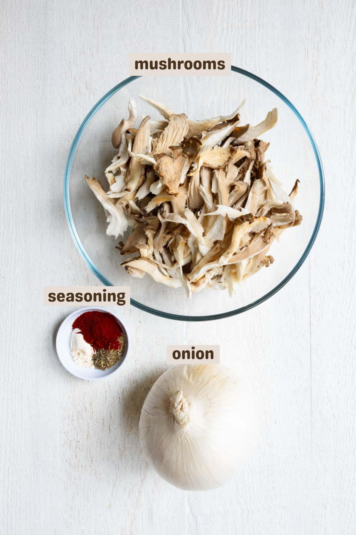 Oyster mushrooms in a glass bowl, an onion, and seasoning.