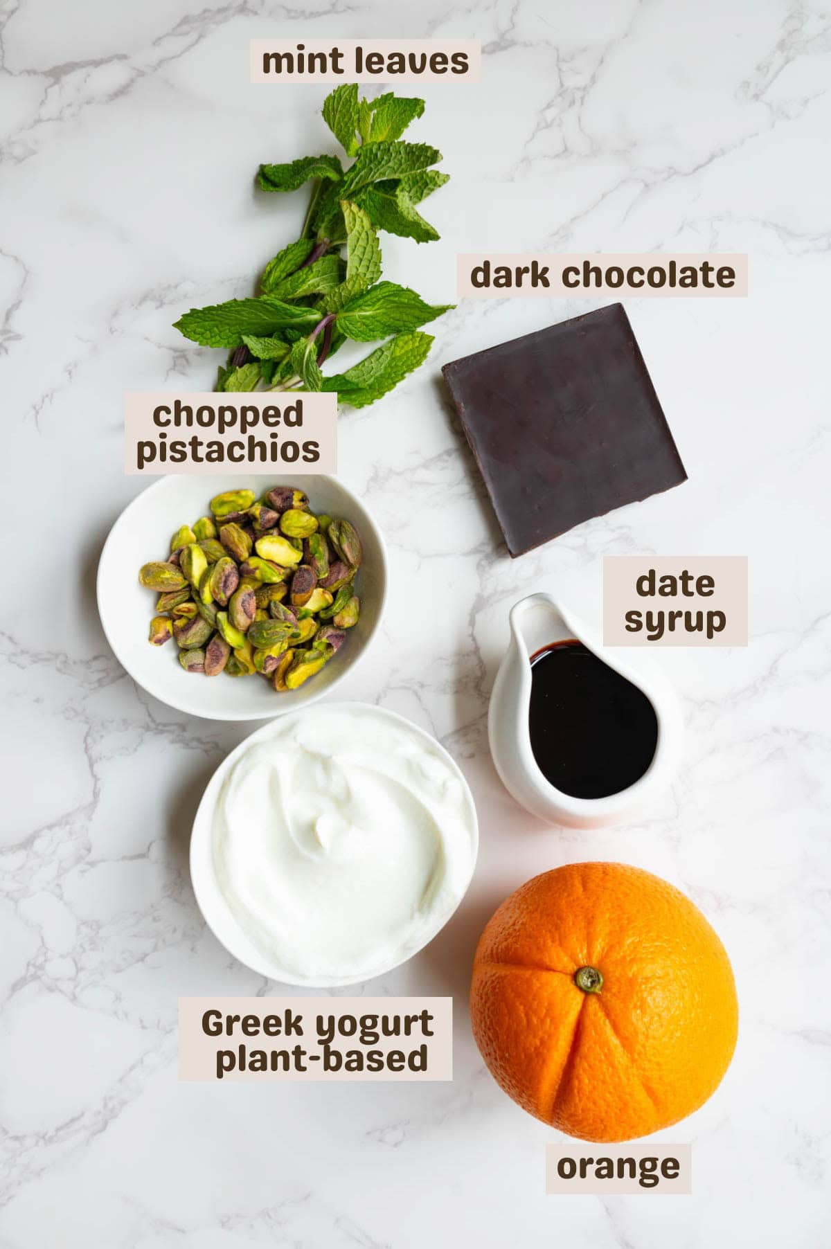Greek yogurt, an orange, dark chocolate, date syrup, pistachios, and mint leaves.