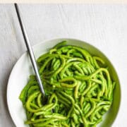 Pasta in green sauce in a white bowl.