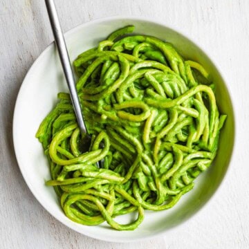 Pasta in green sauce in a white bowl.