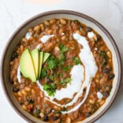 Protein chili with beans in a bowl topped with vegan sour cream, avocado, and chopped fresh herbs.