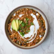 Protein chili with beans in a bowl topped with vegan sour cream, avocado, and chopped fresh herbs.