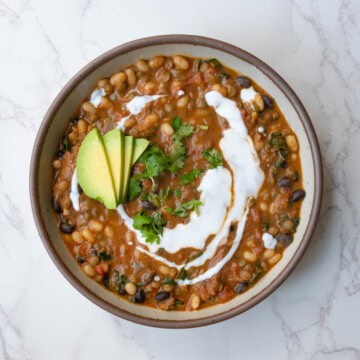 Protein chili with beans in a bowl topped with vegan sour cream, avocado, and chopped fresh herbs.