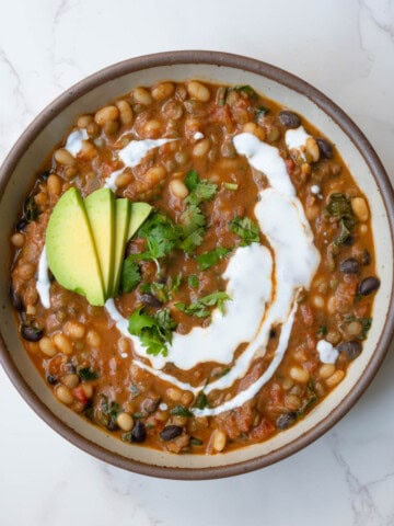 Protein chili with beans in a bowl topped with vegan sour cream, avocado, and chopped fresh herbs.