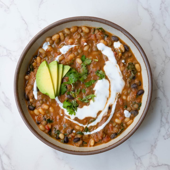 Protein chili with beans in a bowl topped with vegan sour cream, avocado, and chopped fresh herbs.