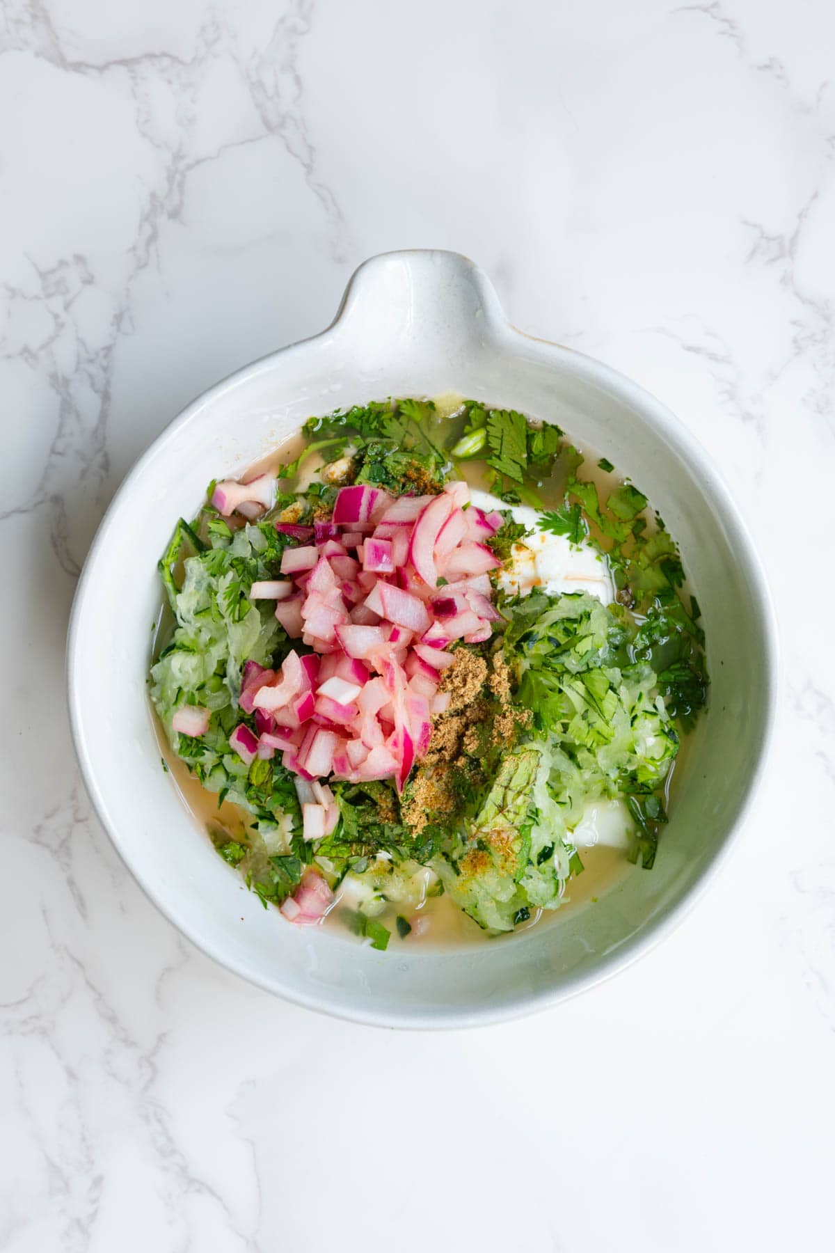 Red onion, Greek-style yogurt, cilantro, date syrup or maple, cucumber, lemon, mint, cumin, and apple cider vinegar in a white bowl.
